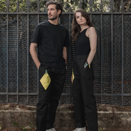 Two models, one male and one female, posing outdoors in casual black clothing with a textured metal fence in the background.